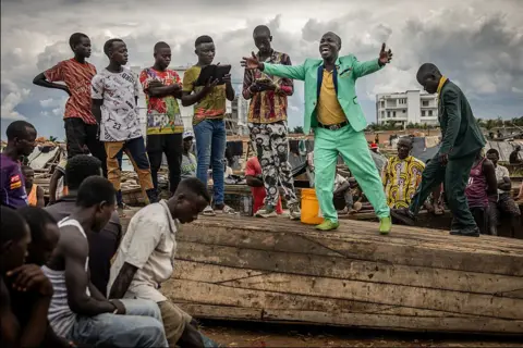 LUIS TATO/AFP A man in a green suit on top of a boat, preaching to a crowd.
