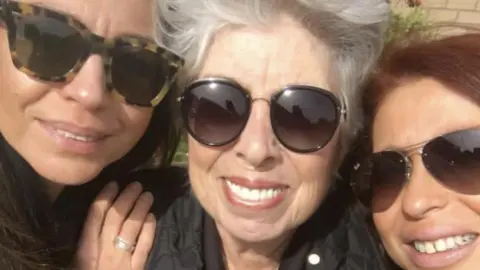 Three women wearing sunglasses smile at the camera.
