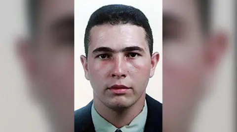 Metropolitan Police/PA Wire Jean Charles de Menezes pictured in a passport-style headshot. He has short black hair, full eyebrows, and wears a dark jacket with a pastel green shirt.