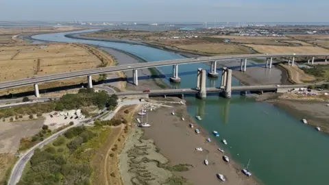 The Sheppey Crossing and Kingsferry Bridge, as seen from above. The landscape on both sides of the water appears yellow and dry.