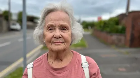 Barbara Arnold is wearing a salmon pink top and has a white backpack