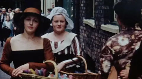 Image from archive footage of women carrying baskets down a street.