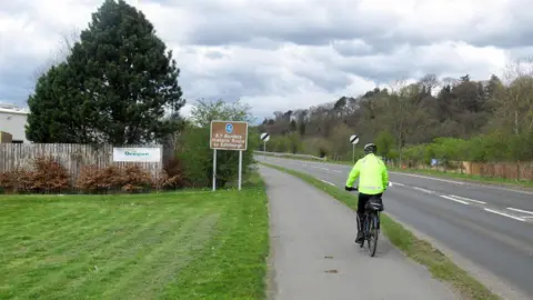Someone on a bike cycling along a pathway next to the A7 in the Borders