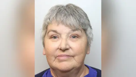 Derbyshire Police A mugshot of Lindsey Foster she has short grey hair and is wearing a purple top and dark jumper