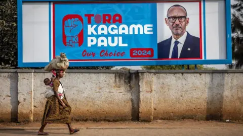 AFP A woman carrying a child on her back walks past an election billboard calling for votes for Rwanda's incumbent President and the ruling Rwanda Patriotic Front (RPF) presidential candidate Paul Kagame in Kigali, July 11, 2024