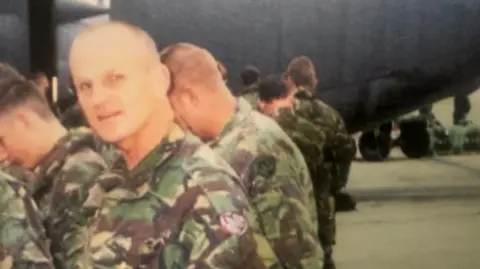 an old picture of a smiling soldier and other soldiers in camouflage uniform