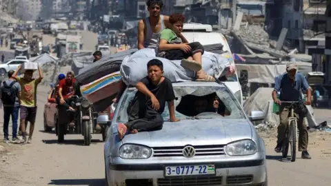 Reuters three children on the top of a turbulent car - one wears black sitting on the hood, and the other - one wears the highest green dishes for the other white jacket - sitting on the bed on the roof. There is a man on a bike to the left, with another on a motorcycle, however, others carry boxes and mattresses along the road of the road with ruins everywhere.