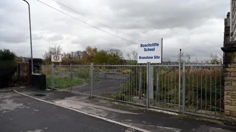 The former site of Branshaw School in Keighley with a blue and white sign and grey fences.