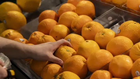 A hand selects an orange at a grocery store