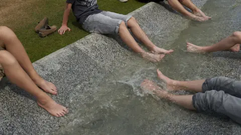 Getty A group of adolescents dip their feet in a fountain. Only their legs are visible.