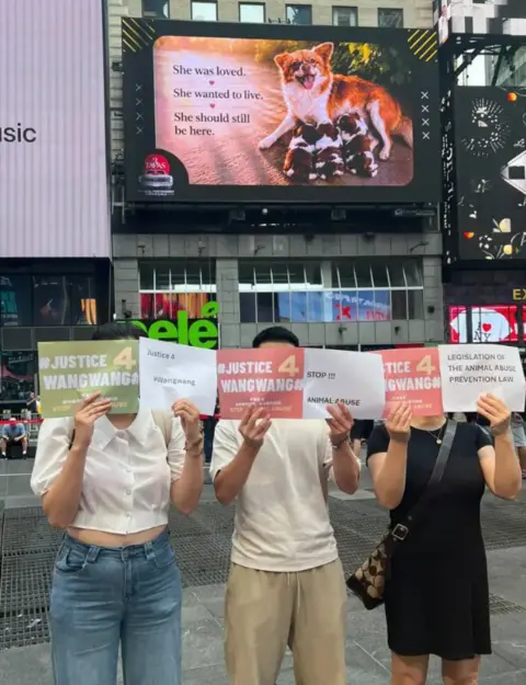 Supplied Three people standing before a billboard of Wang Wang, holding sheets of paper that read, "Justice 4 Wang Wang"