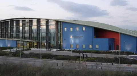 Google The front of the Gloucestershire Constabulary HQ building. It is painted in Blue and terracotta and has a large face of windows.