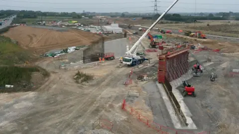 An aerial view of construction of a new bridge taking traffic from the A1079 at the Jock's Lodge junction. The foundation and supporting arms of the bridge can be seen surrounded by cranes and construction crews.