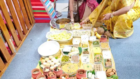 Swindon Hindu Temple Two women are leaning over a display of food in different containers, displayed on a cloth on the floor.