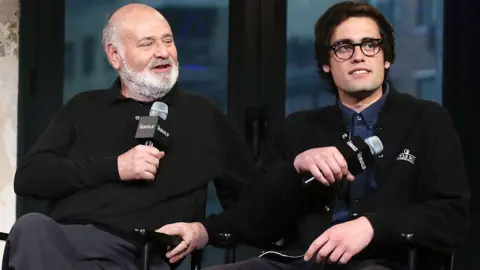 Director Rob Reiner and his son Nick Reiner are seated on a stage while holding microphones during a panel discussion.