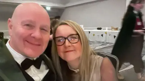 Lee Francis Lee and Clare next to each other at a black tie dinner 