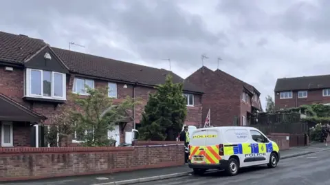 A police van outside a house. A police officer is stood outside the property. 
