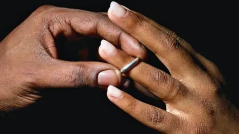 A man places a silver wedding band onto a young woman's ring finger.