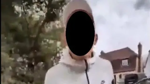 A man in a white, long-sleeved sports top and white cap is pictured facing the camera. Is face is obscured by a black circle. 