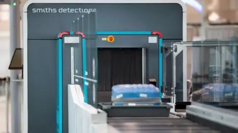 Smiths Detection A Smiths Detection airport security scanner with a blue suitcase in a tray on the conveyor belt.
