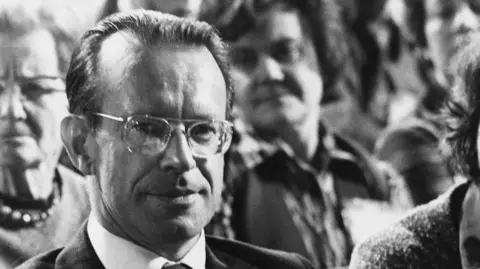 Black and white image of Joe Haines at the 1977 Conservative Party Conference, wearing impassive expression