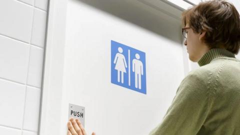 A person opens a toilet door with both male and female sign on it