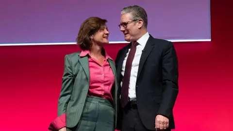 Getty Images Eluned Morgan wearing a grey suit and pink shirt has her arm around Keir Starmer who is wearing a dark suit, white shirt and a dark red tie. They are smiling at one another