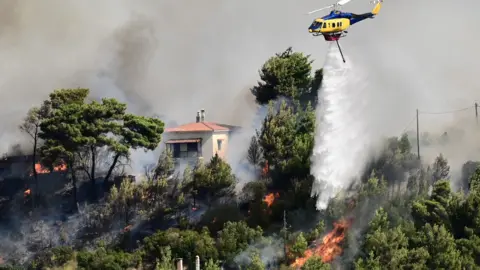 Reuters Een helikopter vliegt voorbij en laat water vallen op een vuur dat vlakbij een huis brandt