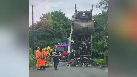 A lorry with burnt waste spilling out on to a village road