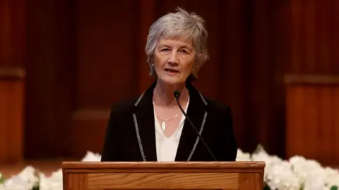 Catherine Connolly speaking into a microphone. She is wearing a white top and a black suit jacket. 