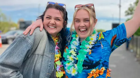 Two women dressed in bright clothes and floral garlands around their necks celebrate