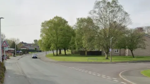 Google Maps A car is driving along Unicorn Road before a junction. Trees and grass surround some housing on the right side of the street