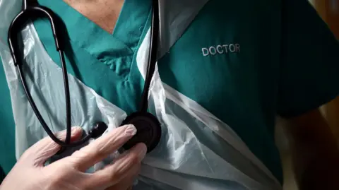 A turquoise doctor's uniform with a PPE apron draped across the front. A stethoscope is around his neck.