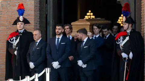 Antonio Masiello/Getty Images Uniformed pallbearers carry the coffin of Valentino Garavani from the basilica as guards stand on either side