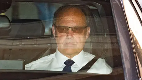 PA Media Glyn Razzell leaving the High Court hearing the passenger seat of a car. He is wearing a white shirt, black tie and tinted glasses.