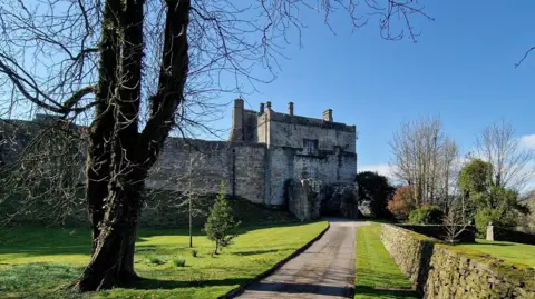 A driveway surrounded by a manicured lawn leads up to the entrance to Cockermouth Castle. 