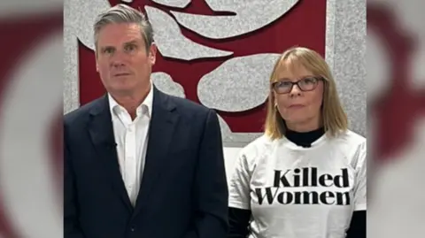 Julie Devey Julie wearing a t-shirt with the words Killed Women on it. She is stood next to Prime Minister Kier Starmer. Both are looking into the camera.