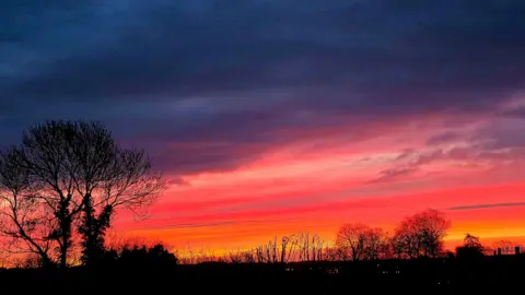 ALFIE COLE/WEATHERWATCHERS Rich hues of purple, pink, orange and yellow fill the sky above Irthlingborough and silhouette nearby trees.