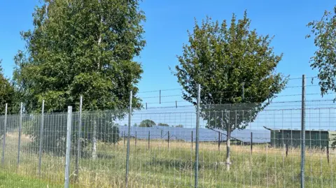 Solar panels in a field behind a grey fence