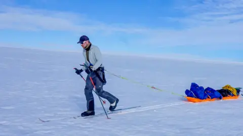 Sebastian Gjolstead Frederick Fennessy on skis pulling a sled across snow - there is only snow and blue sky visible in the background.