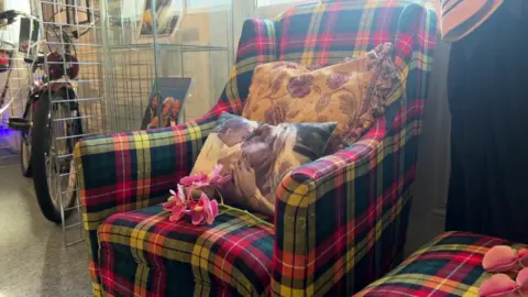 The armchair is in bright tartan. It has a cushion on it with a picture of Dwina.