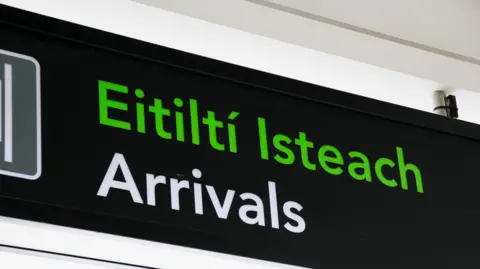 Getty Images Arrivals sign at Dublin airport. Arrivals is written in green in Irish, and below in English in white, on a black sign. 