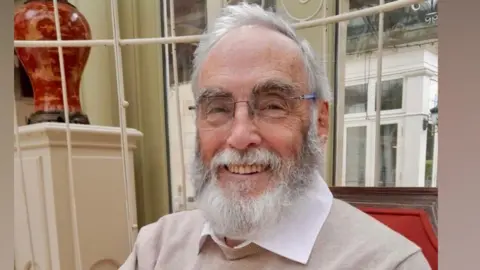 Picture of Philip Blundell. He has grey hair and beard and is smiling. He is wearing a while shirt under a 