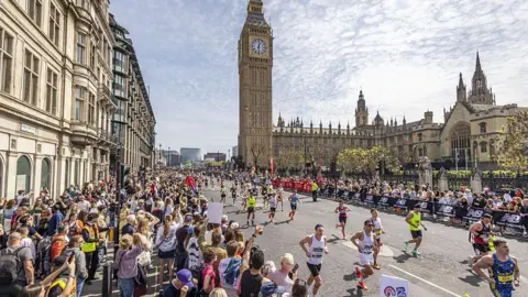 Getty Images Runners can be seen with supporters on either side of the road behind barriers. Some hold signs, others have drinks in their hands. In the background you can see Big Ben attached to the Houses of Parliament.