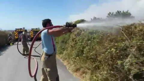 A firefighter spraying a hedge at the Lands End airport fire. 