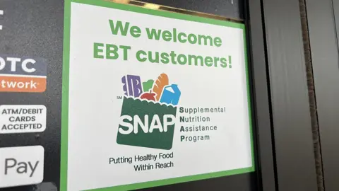 A sign on the window of a store reads "We welcome EBT customers", along with a logo for Snap.