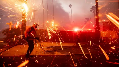 Sparks and debris fly as a firefigher tackles the blaze in Pacific Palisades on 7 January