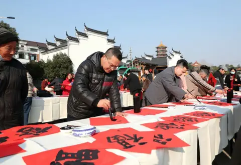 Bao Kangxuan/VCG melalui Getty Images Penggemar kaligrafi menulis karakter Tionghoa 'Fu' yang berarti keberuntungan, untuk menyambut Tahun Baru 2025 pada 31 Desember 2024 di Jinhua, Provinsi Zhejiang, Tiongkok. 