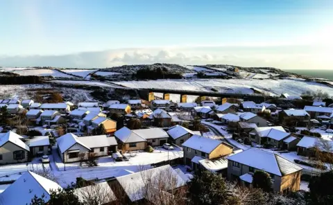 BBC Weather Watchers/slynchie Snowy rooftops from above with snowy hills in the background.