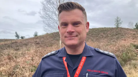 Tim Kench smiling at the camera is in his navy blue fire and rescue with red lanyard.